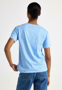 Vaaleansininen lyhythihainen t-paita, joka on valmistettu puuvillasta. Paitassa on pyöreä kaula-aukko, rento istuvuus ja sileä pinta. Takana yksinkertainen muotoilu.