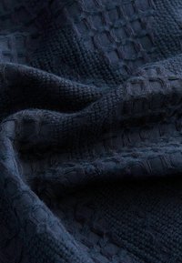 Tejido texturizado azul marino con un patrón tejido de cuadrados en relieve y un acabado suave, que resalta su profundidad y diseño intrincado.