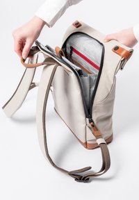 Beige Tasche mit mehreren Taschen, braunen Lederdetails, Reißverschluss, verstellbaren Riemen und einem karierten Innenfutter mit rotem Reißverschluss.