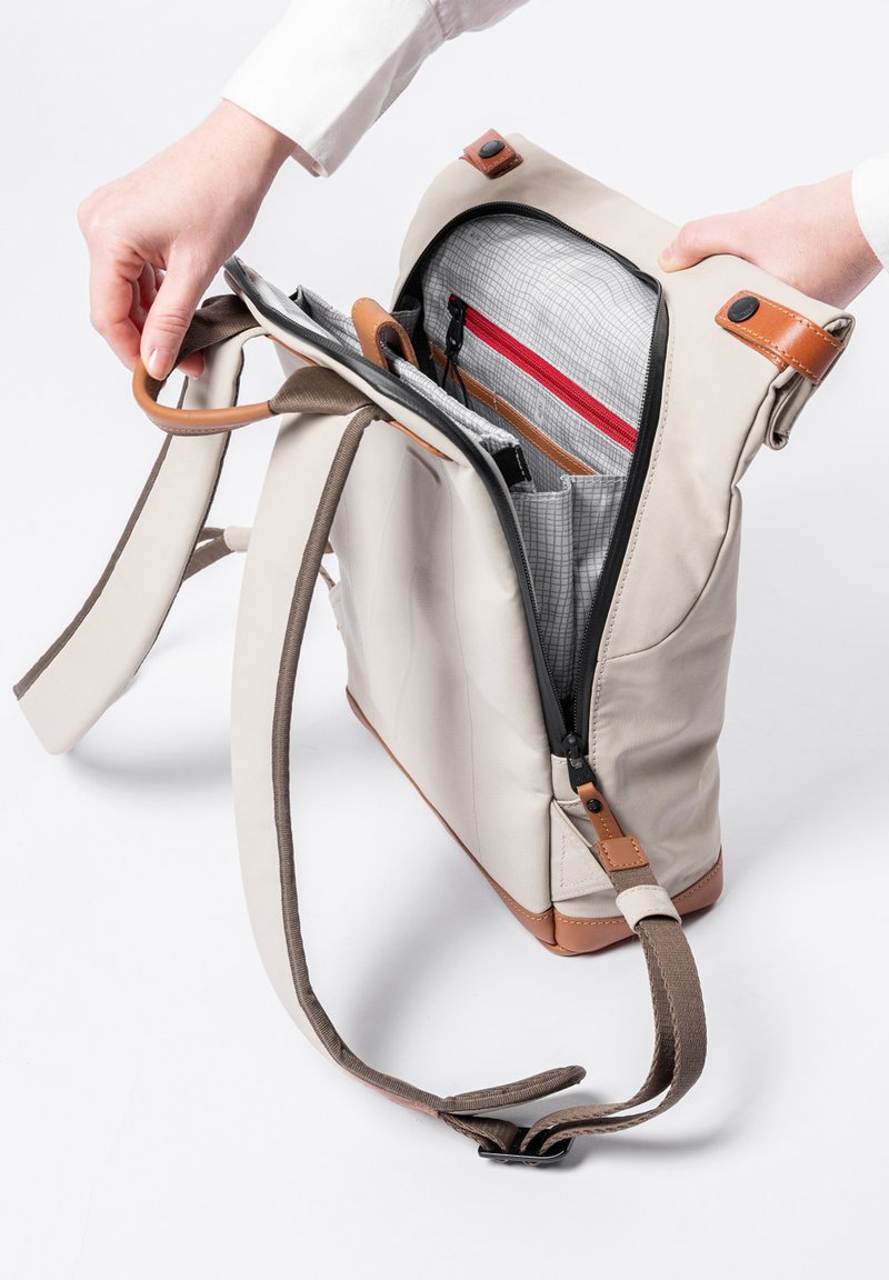 Beige Tasche mit mehreren Taschen, braunen Lederdetails, Reißverschluss, verstellbaren Riemen und einem karierten Innenfutter mit rotem Reißverschluss.