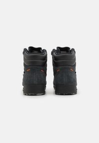 Zapatos de ante negro de media caña con acentos de goma, un acabado texturizado y una suela con patrón. Presentan un cuello acolchado y cierre de cordones.