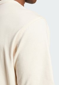 Krémová, mäkká bavlnená tričko s okrúhlym výstrihom a viditeľným švom na pleciach. Hladká textúra, priliehavý strih.