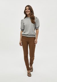 Grå puffärmad sweatshirt i kombination med bruna slim-fit byxor och gröna remsandaler. Modellen står framför en neutral bakgrund.
