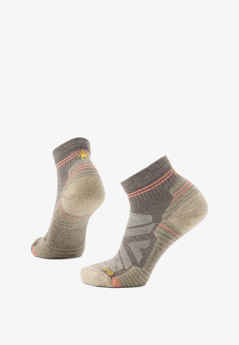 Par de calcetines deportivos de corte bajo en beige y gris con detalles en naranja, que cuentan con refuerzos en el talón y la punta.