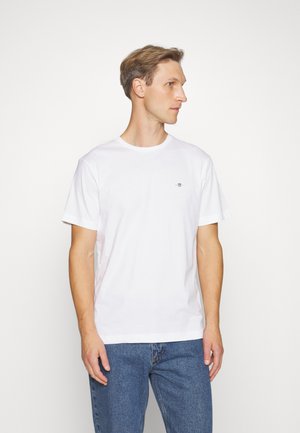 Hvit bomull T-skjorte med rund hals, korte ermer og en liten logodetalj på brystet. Kombinert med blå denimjeans.