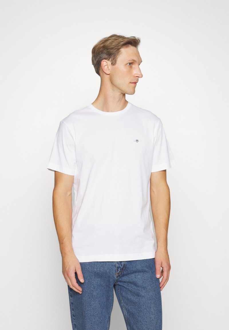 Hvit bomull T-skjorte med rund hals, korte ermer og en liten logodetalj på brystet. Kombinert med blå denimjeans.