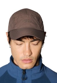 Brun keps i lätt material med sömnadsdetaljer och texten "HALO off-duty" på framsidan. Strukturerad skärmdesign.