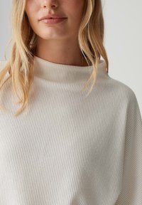 Crèmekleurige geribde trui met een hoge hals en een ontspannen pasvorm, met een zachte textuur en subtiele verticale strepen.