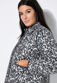 Leopardmønster jakke i sort og hvid, med krave, kontrastkanter og sidelommer. Letvægtsstof med en glat tekstur.