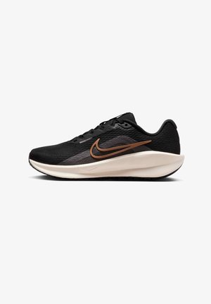 Zapatilla de running negra con una parte superior de malla transpirable, que presenta un diseño texturizado, el logo Nike en bronce y una entresuela acolchada en color crema.