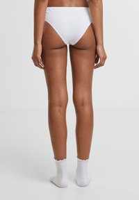 Bijele pamučne gaćice s niskim strukom, s glatkim rubovima i minimalnom pokrivenošću. Nosive s bijelim čarapama s volanima do gležnja.