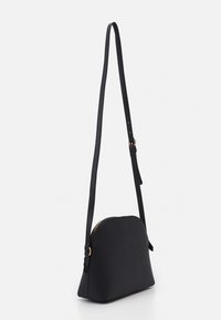 Černá kožená crossbody taška s zakřiveným siluetou, zlatým zipem a jedním nastavitelným popruhem pro všestranné možnosti nošení.