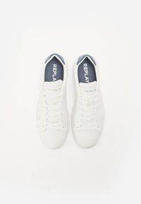 White sneakers with a smooth leather finish, featuring a perforated design, blue insoles, and prominent “REPLAY” branding on the tongue.