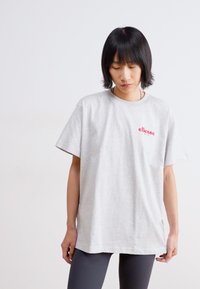 Šedé bavlněné tričko s krátkým rukávem, s malým červeným logem "ellesse" na přední straně, volný střih a jednoduchý design.