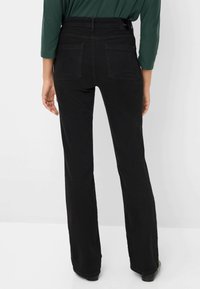 Jeans neri a campana con vita alta, dotati di due tasche posteriori e un tessuto liscio e testurizzato. Progettati per una silhouette aderente.