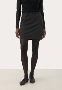 Schwarzes Spitzenoberteil mit langen Ärmeln, kombiniert mit einem grauen karierten Miniröck. Der Rock hat eine enganliegende Silhouette und ein dezentes Karomuster. Dazu werden schwarze Strumpfhosen und Ballettschuhe getragen.