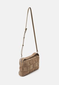 Sac à épaule en daim beige avec un design tissé, un haut incurvé et une bandoulière amovible. Présente des éléments en métal argenté et une texture douce.