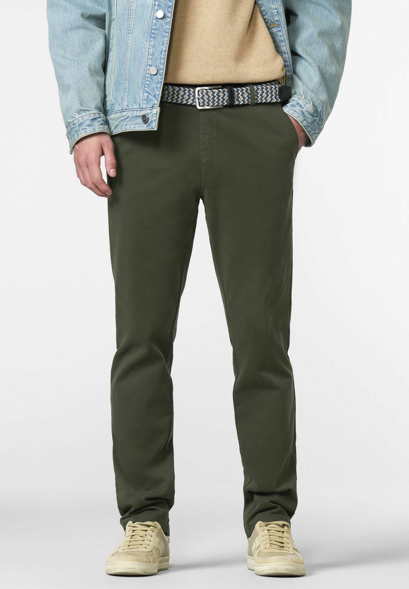 Chinos verde oliva in taglio slim, con vita piatta e tasche laterali, abbinati a sneakers beige e una cintura intrecciata a fantasia.