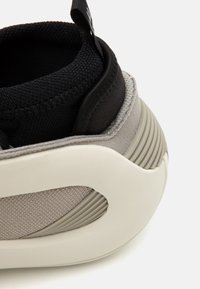 Szaro-czarne sneakersy z teksturowanym cholewką, gumową podeszwą z poziomymi rowkami oraz pętelką na kostce ułatwiającą zakładanie.