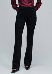 Pantalones acampanados negros hechos de una tela elástica, con una cintura alta y diseño sin costuras, combinados con tacones negros puntiagudos.