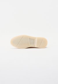 Sål i tan gummi med et strukturert mønster, som har spor og kanter for grep, plassert mot en hvit bakgrunn.