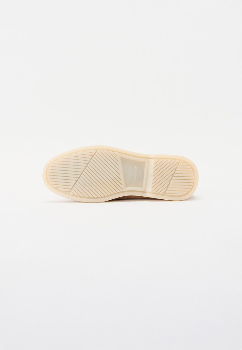 Semelle de chaussure en caoutchouc beige avec un motif texturé, comportant des rainures et des nervures pour une meilleure adhérence, sur fond blanc.