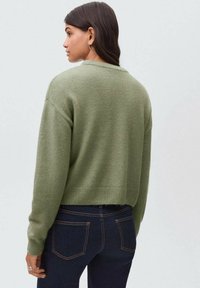 Kratki zeleni džemper od mekog materijala s okruglim izrezom, spuštenim ramenima i rebrastim rukavima, uparen s tamnim trapericama.