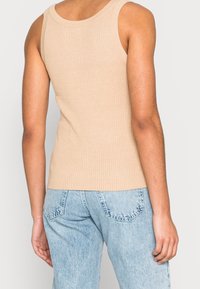 Béžová žebrovaná tílko s širokými ramínky, přiléhavý střih a délka do boků, spojené se světle modrými džíny.