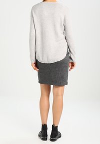 Jersey gris claro con un dobladillo redondeado, combinado con una falda ajustada con estampado en blanco y negro. La modelo lleva botas negras hasta el tobillo.