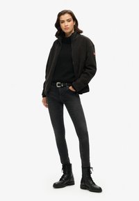 Giacca in pile nera con zip frontale, indossata sopra un maglione nero. Abbinata a jeans skinny neri e stivali da combattimento neri con lacci.