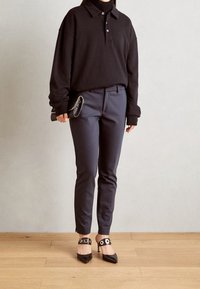 Czarna, oversize'owa długa koszulka polo z długim rękawem, granatowe, dopasowane spodnie oraz czarne szpilki z okrągłymi ozdobami przy palcach. Minimalistyczny design.