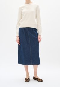 Ljust beige tröja med ribbade mudd, tillsammans med en mörkblå denimkjol med rak passform och synlig sömnad. Leopardskifts-flatsskor.