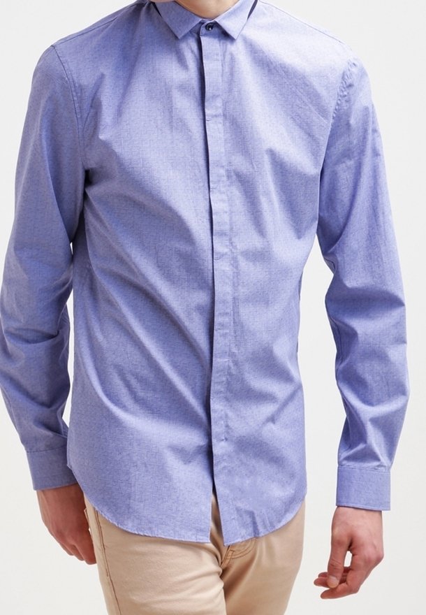 Koszula na guziki z długim rękawem w jasnoniebieskim kolorze o subtelnej fakturze, z kołnierzem i prostym dołem, noszona z beżowymi spodniami.