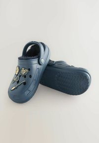 Donkerblauwe klompen met een zachte binnenkant, voorzien van decoratieve bedels bovenop, ventilatiegaten en een gestructureerde rubberen zool voor grip.