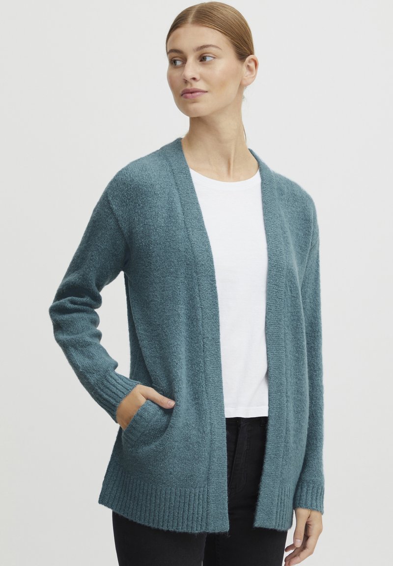 Turkos cardigan i mjukt, texturerat material. Öppen framsida med långa ärmar och ribbade manschetter. Inkluderar två framfickor.