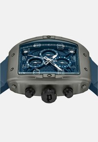 Zilveren roestvrijstalen horloge met een rechthoekige blauwe gestructureerde wijzerplaat, drie subdials, zilveren uurmarkeringen en zwarte drukknoppen. Blauwe rubberen band.