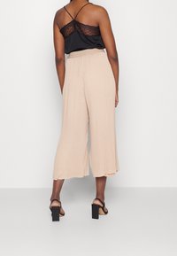 Svart spetskantad linne kombinerad med beige, veckad culotte-byxor. Outfiten har en avslappnad passform och svarta högklackade sandaler.