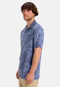 Kurzärmliges Hemd in Blau mit einem hellkorallenfarbenen Muster, ausgestattet mit einer Brusttasche und einem lockeren Schnitt. Strukturierte Stoffoberfläche.