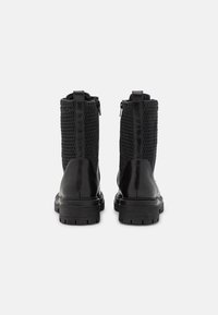 Botines negros que presentan una base de piel lisa y parte superior de malla, con un zipper en el lateral y una suela de goma resistente.