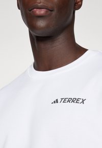 White sweatshirt made of smooth fabric with a round neckline. Features a black "TERREX" logo on the chest and subtle stitching details.