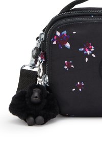 Black fabric bag with small purple, pink, and blue floral patterns and a black plush gorilla keychain attached near the zipper.