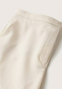 Pantalon beige à la texture lisse et au design sur mesure avec une poche latérale et une ceinture structurée. Le matériau semble léger et doux.