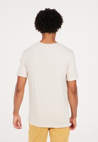 Camiseta de manga corta en color beis claro con cuello redondo y corte relajado. Tejido texturizado con un sutil patrón jaspeado.