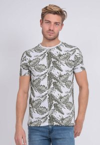 T-shirt à manches courtes en tissu gris clair avec un motif floral vert, col rond et design ajusté, associé à un jean en denim bleu.