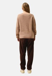 Beżowy sweter z prążkowanej dzianiny o luźnym kroju, w połączeniu z ciemnobrązowymi spodniami z kordurowej tkaniny. Model ma na sobie kremowe sneakersy.