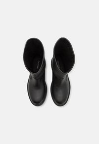 Paire de bottes en cuir noir mi-mollet avec des bouts arrondis et des coutures visibles, vues de dessus sur un fond blanc.