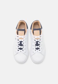 Valkoiset urheilukengät tummansinisillä yksityiskohdilla. Lycroyhkeäpintainen yläosa, pyöreä kärki ja litteät nauhat. Pehmustettu nilkkaosa ja kieli brändiyksityiskohdalla.