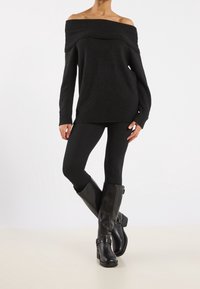 Černý svetr bez ramínek s žebrovaným výstřihem, spárovaný s černými legínami a koženými vysokými botami s přezkou.