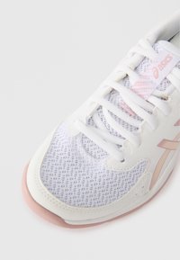 Λευκό αθλητικό παπούτσι με ροζ λεπτομέρειες, διαθέτοντας δικτυωτό άνω μέρος, στρογγυλή μύτη, κλείσιμ ο με κορδόνια και καουτσούκ σόλα. Μαλακή υφή και ρευτή σχεδίαση.