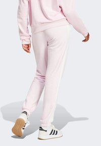 Pantaloni della tuta rosa con strisce bianche sui lati, polsini affusolati e una consistenza morbida. Abbinati a sneakers bianche con strisce nere.